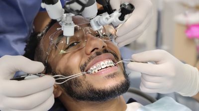 Orthodontist placing traditional metal braces on teenage patient in contemporary dental office