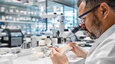 Skilled dental technician in Tijuana laboratory examining custom-made clear aligners with precision magnification glasses and specialized instruments.